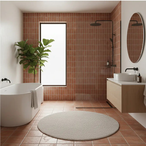 Modern bathroom featuring earthy terracotta floor and wall tiles, a white soaking tub, and minimalist black fixtures for a contemporary organic look.
