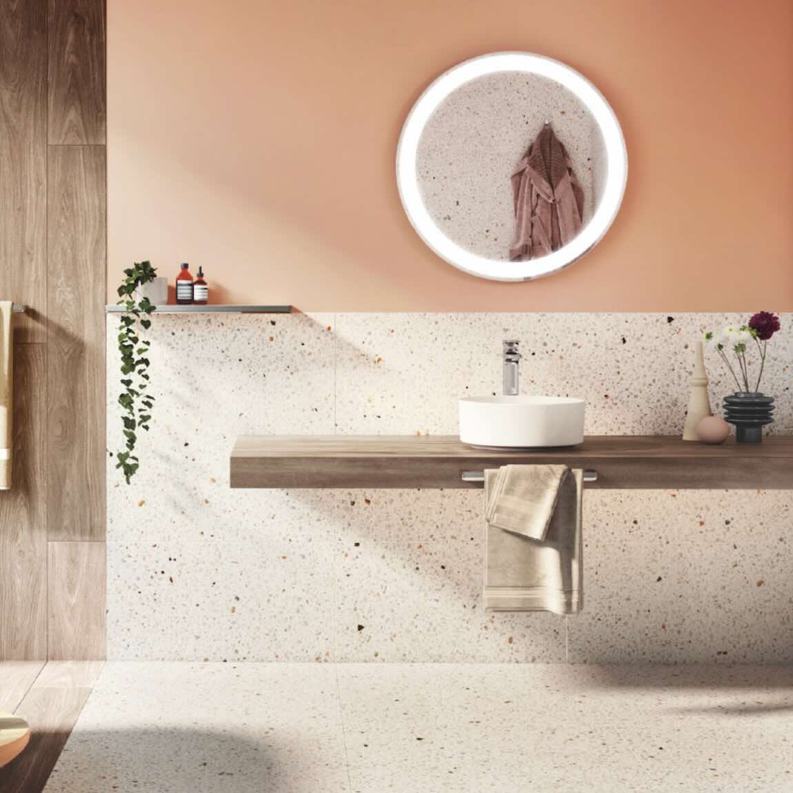 Modern salmon bathroom with a round mirror, sink, terrazzo porcelain tiles, and decorative elements.