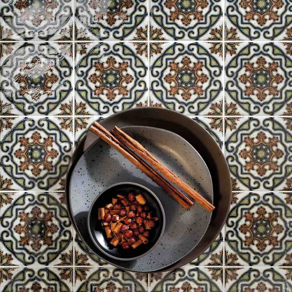 Decorative tiles with a bowl of nuts and cinnamon sticks on a patterned surface