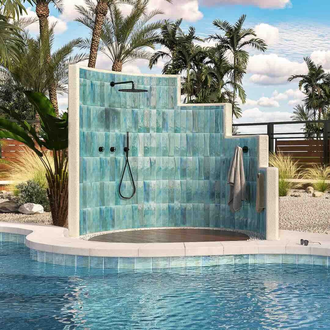 Outdoor shower with blue tiled wall next to a pool, surrounded by palm trees.