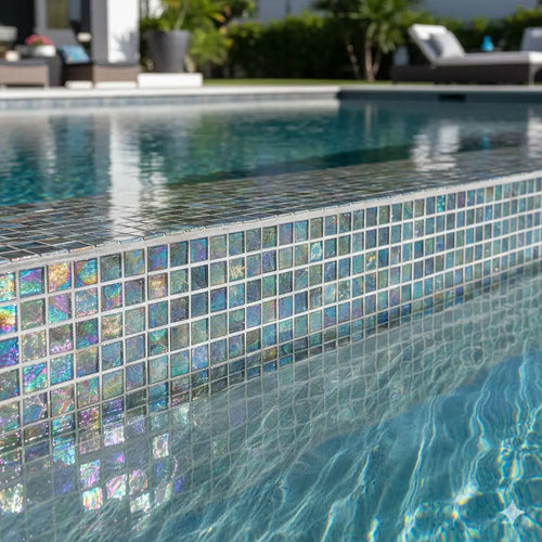 Close-up of shimmering iridescent glass mosaic tiles used on a luxury swimming pool waterline, reflecting sunlight in turquoise water.